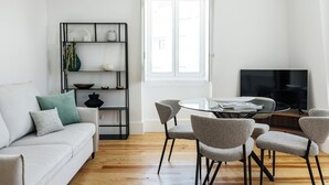 Een moderne woonkamer met een bank, een eettafel met glazen blad en een televisie.