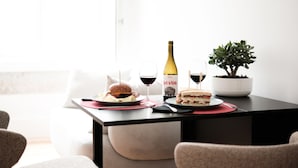Een eettafel met een fles wijn, twee sandwiches en een potplant.