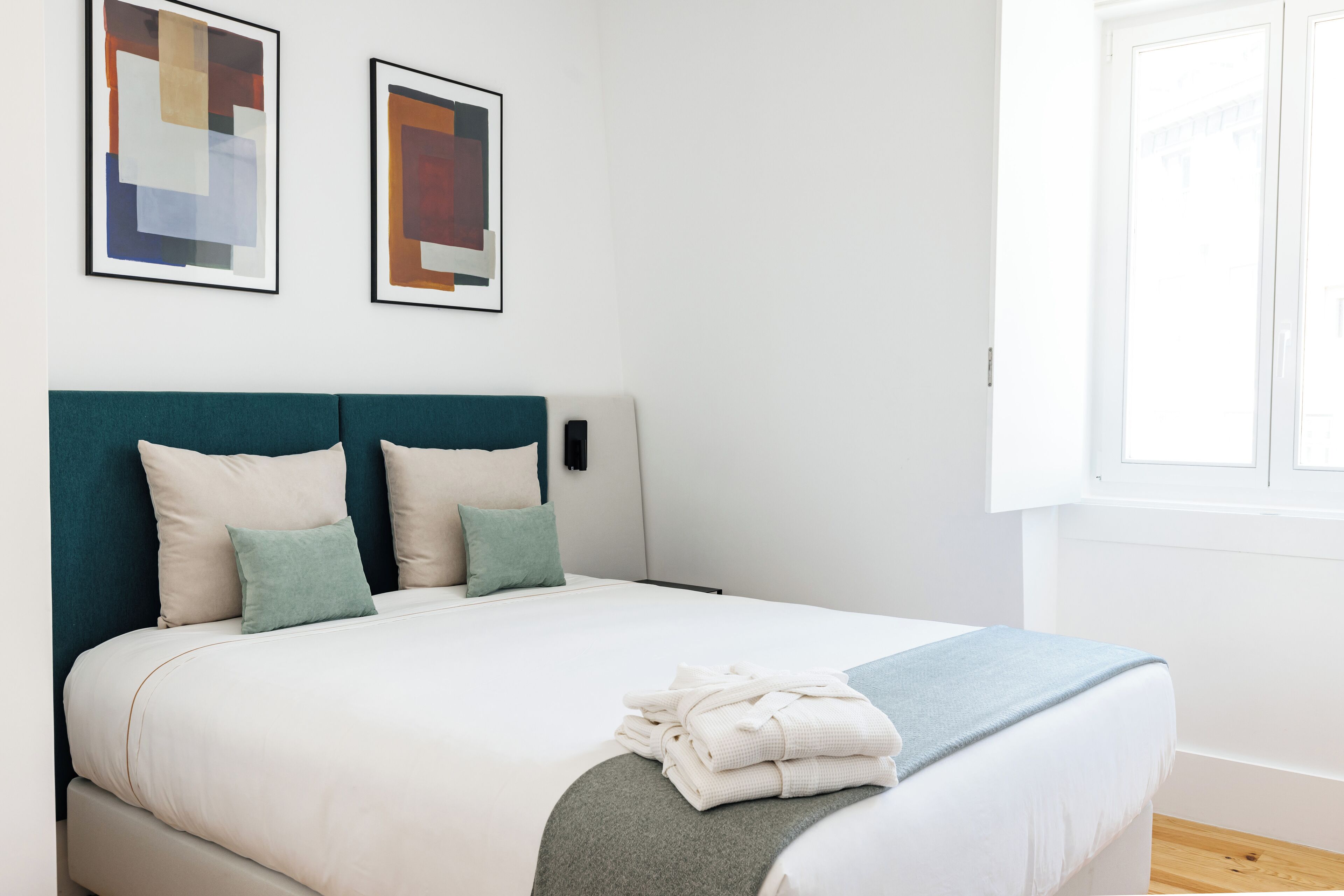 A neatly made bed with a teal headboard, white bedding, and a folded towel on the footboard.