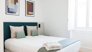A neatly made bed with a teal headboard, white bedding, and a folded towel on the footboard.