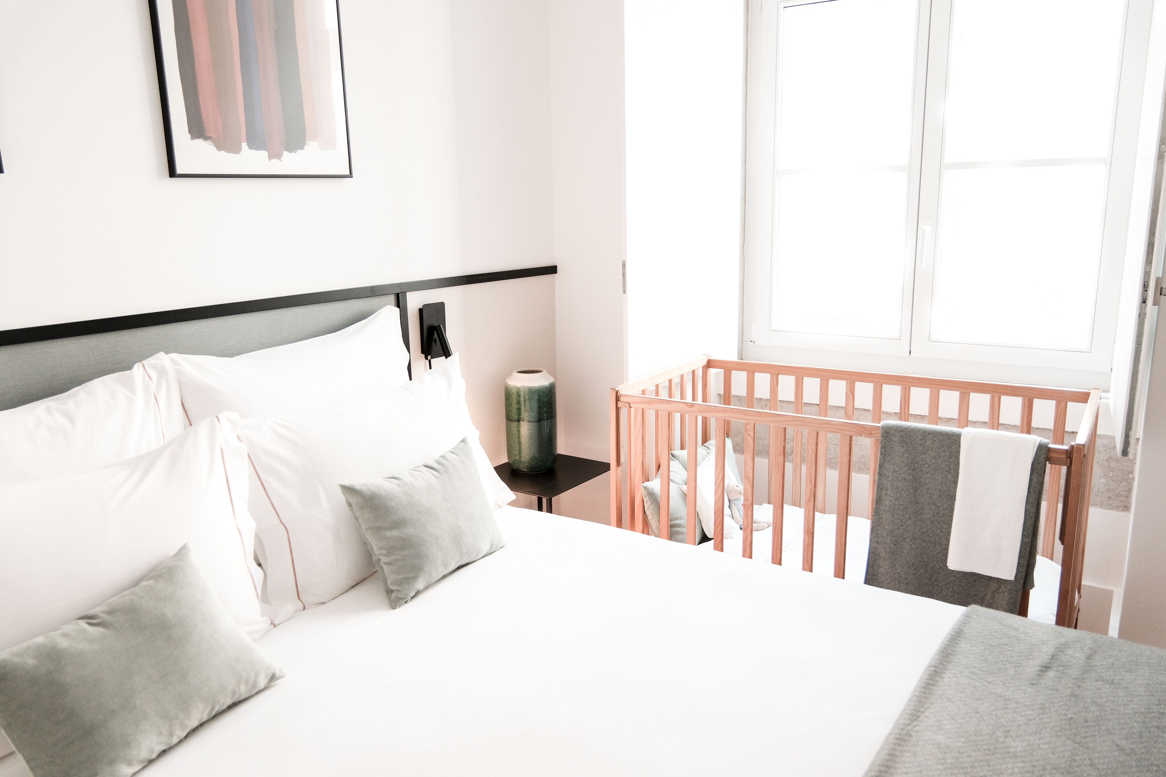 Een hotelkamer met een groot bed, een ledikantje, een nachtkastje en een raam.