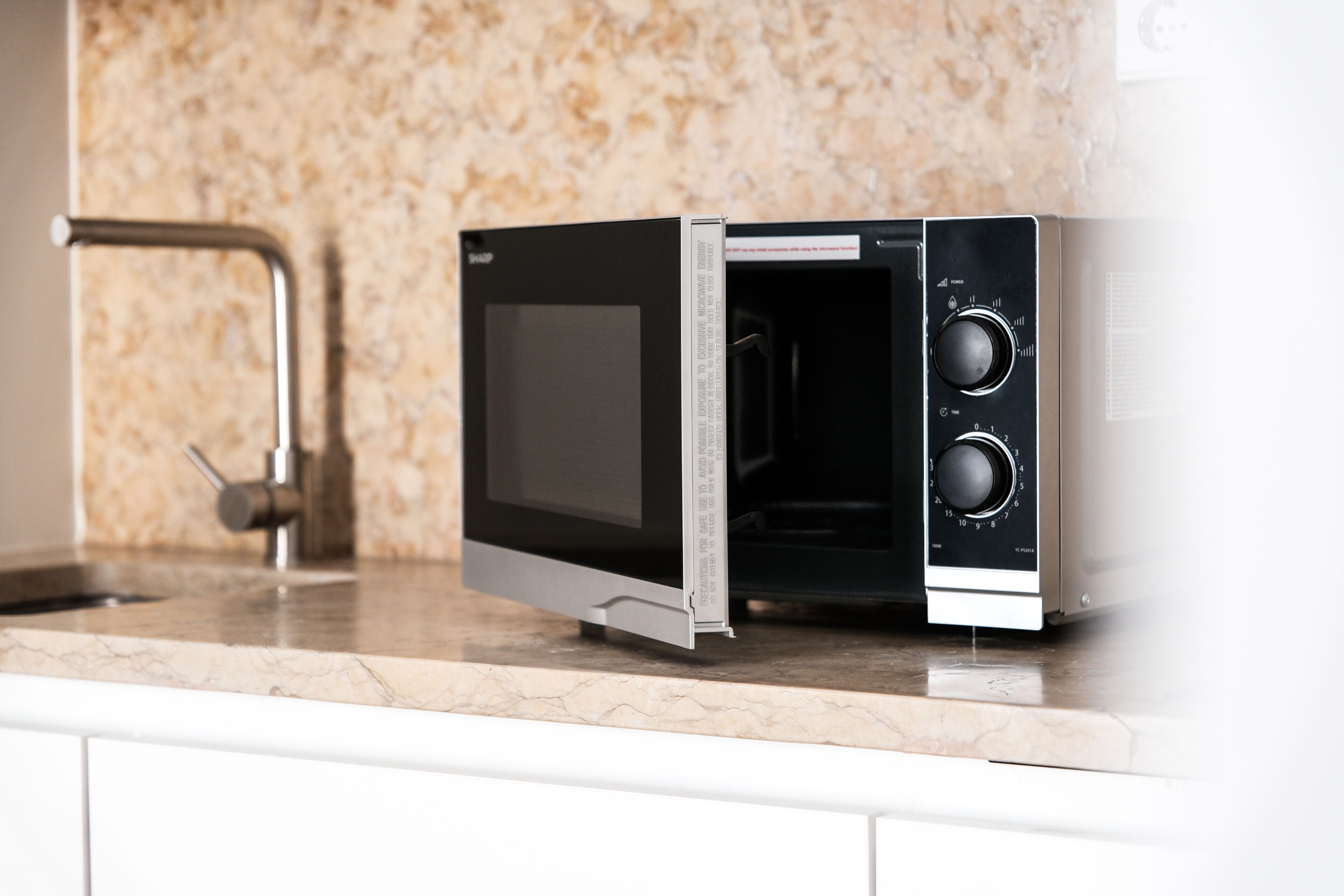 A kitchen with a microwave on a marble countertop, a stainless steel faucet, and a granite backsplash.