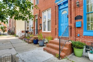 A row of red brick townhouses with blue doors and windows, a sidewalk, and potted plants. - Quirky Baltimore Townhome ~ 2 Mi to Inner Harbor (Baltimore)