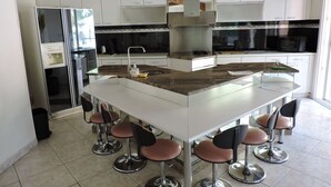 Una cocina moderna con armarios blancos, una isla central con taburetes y electrodomésticos de acero inoxidable.