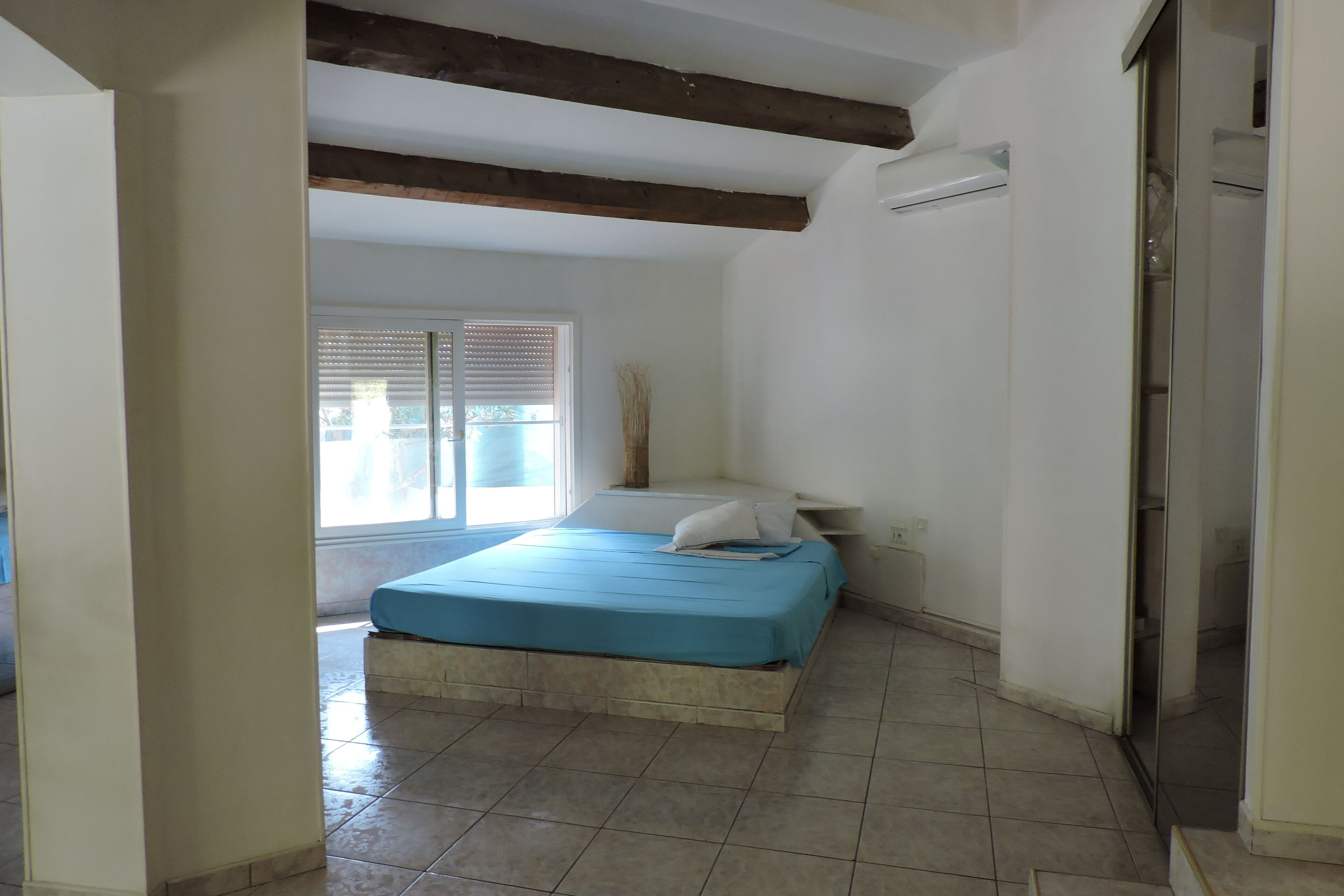 A bedroom with a bed, a window with blinds, a door, and a tiled floor.