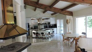 Una cocina amplia con una isla central, taburetes de bar y un comedor con mesa y sillas blancas.
