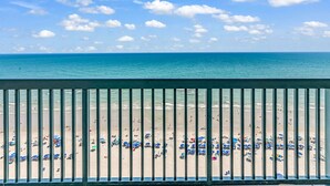 Une plage avec des parasols et des gens, vue depuis un balcon doté de rampes en métal.