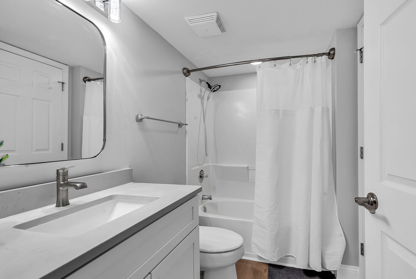 Une salle de bain moderne avec un lavabo blanc, un miroir et des toilettes, une douche avec un rideau et une baignoire.