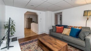 Ein Wohnzimmer mit grauem Sofa, einem Holztisch und einem Fernseher auf einem Schrank.