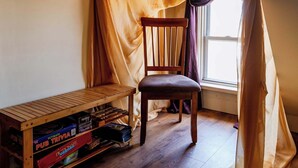 A corner room with a wooden chair, a small table, and a window with sheer curtains.