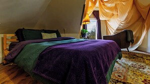 A bedroom with a bed, a chair, a window with curtains, and a lamp.