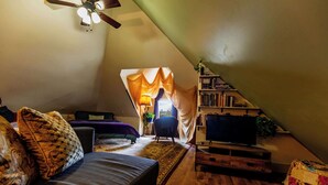 A cozy attic bedroom with a sloped ceiling, a bed, a sofa, a TV, and a bookshelf.