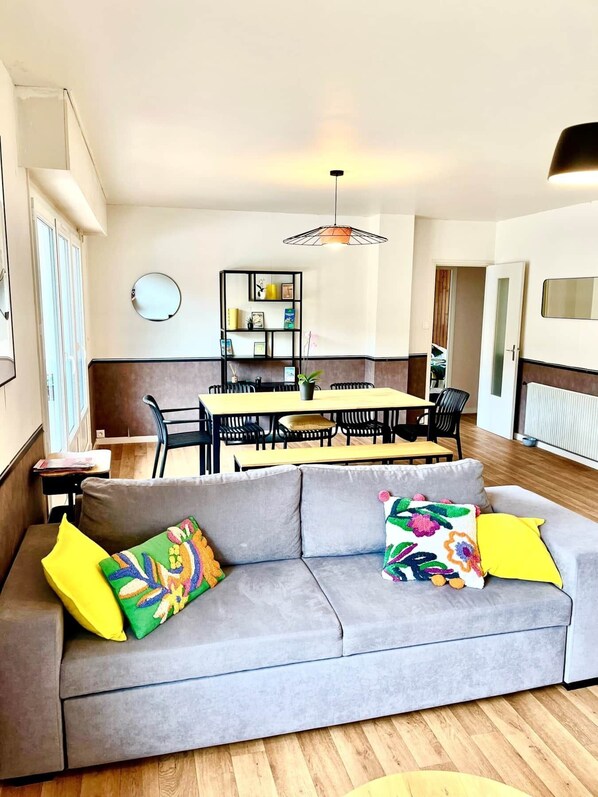 A modern living room with a grey sofa, colorful cushions, a dining area with a table and chairs, and a pendant light. - Traezh Ar Vag - Apartment Beach Perros-Guirec (Perros-Guirec)