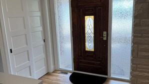 Ein Zimmer mit Holztür, geätzten Glasscheiben, einer schwarzen Fußmatte und einem hellen Boden.