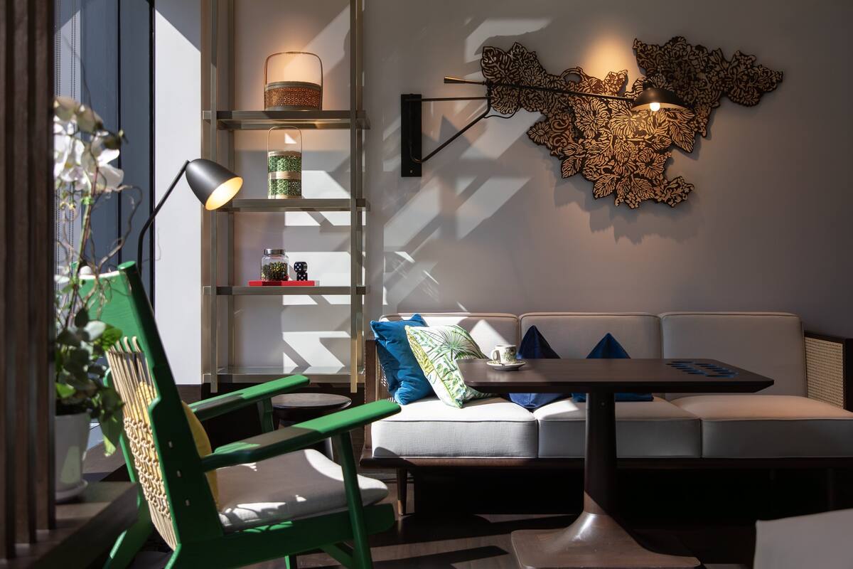 A modern living room with a green chair, a white sofa, a small table, and a wall-mounted lamp.