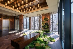 A modern lobby with a wooden bench, hanging light fixtures, and a brick wall with a green plant arrangement. - Hotel Indigo Kuala Lumpur On The Park by IHG (Kuala Lumpur)