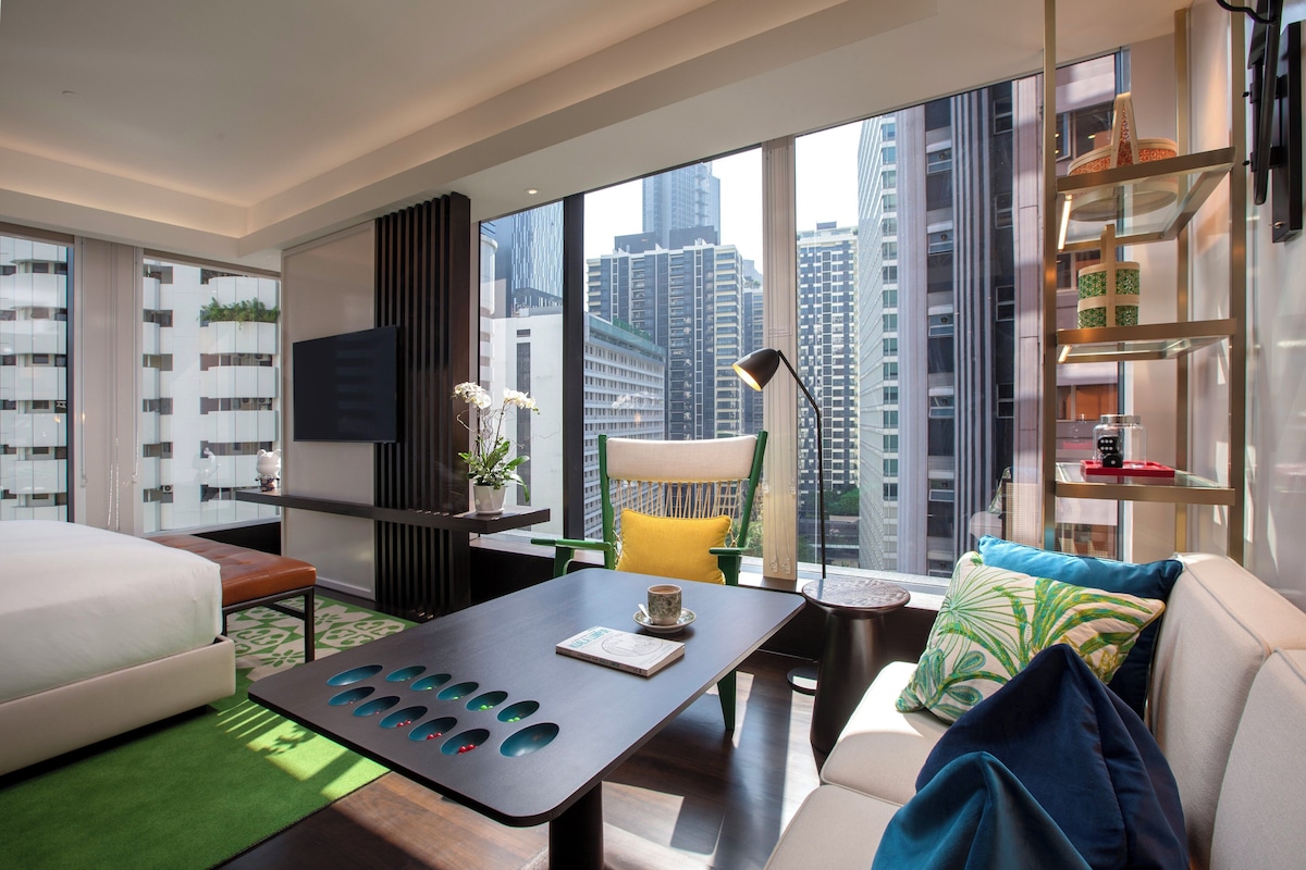 Une chambre d’hôtel moderne dotée d’une grande fenêtre, d’un canapé, d’un lit, d’une table basse et d’un téléviseur.