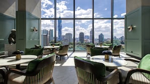 Un espace de restauration moderne avec des tables rondes et des chaises recouvertes d’un tissu vert, ainsi que de grandes fenêtres offrant une vue sur la ville.