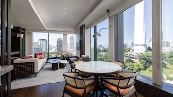 A spacious living room with a round table and chairs, a sofa, and a view of the cityscape through large windows.