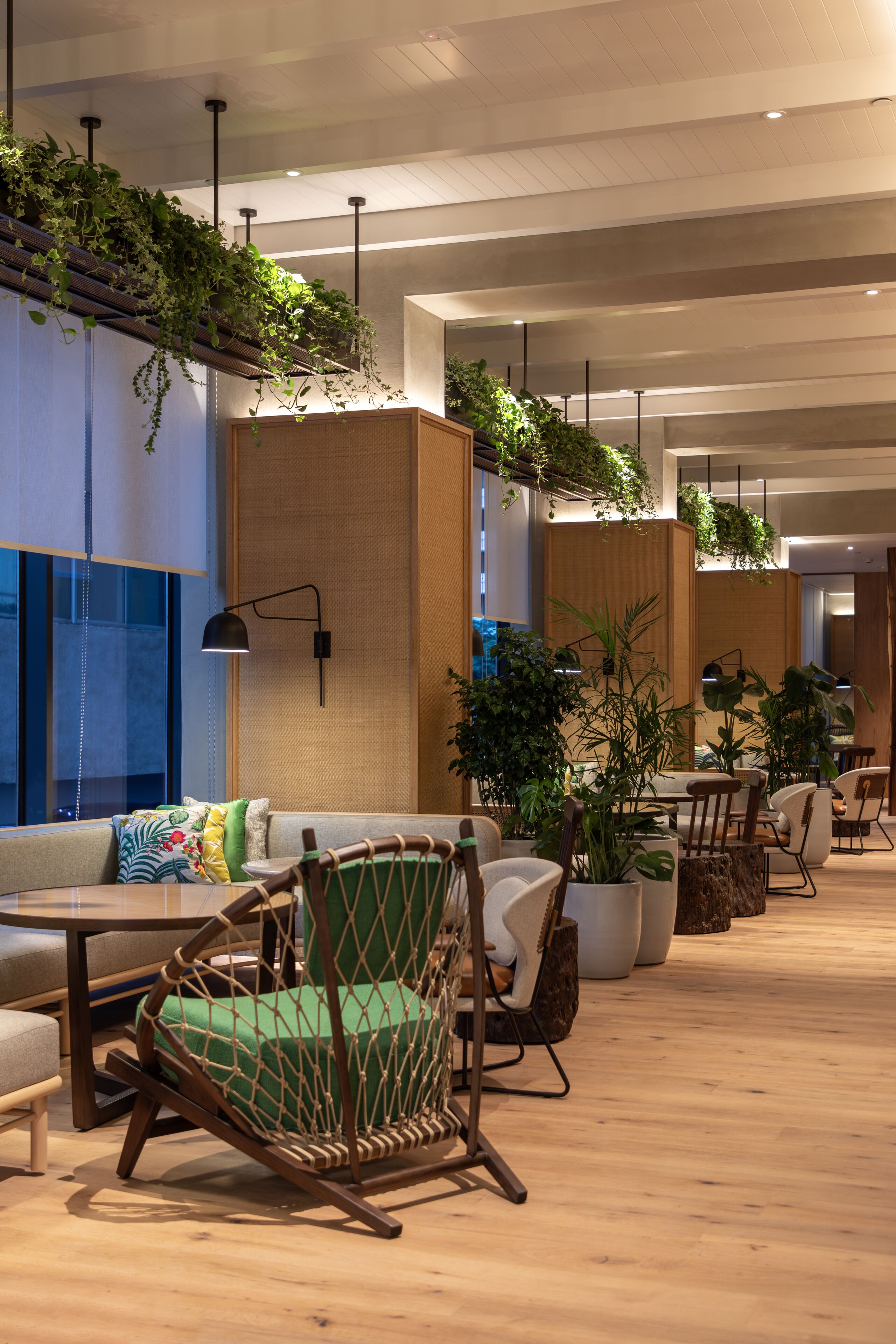 A modern interior with seating areas, wooden floors, and hanging plants.