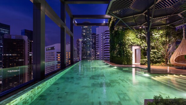 Une piscine sur le toit offrant une vue sur la ville, entourée de verdure et bordée d’une architecture moderne.