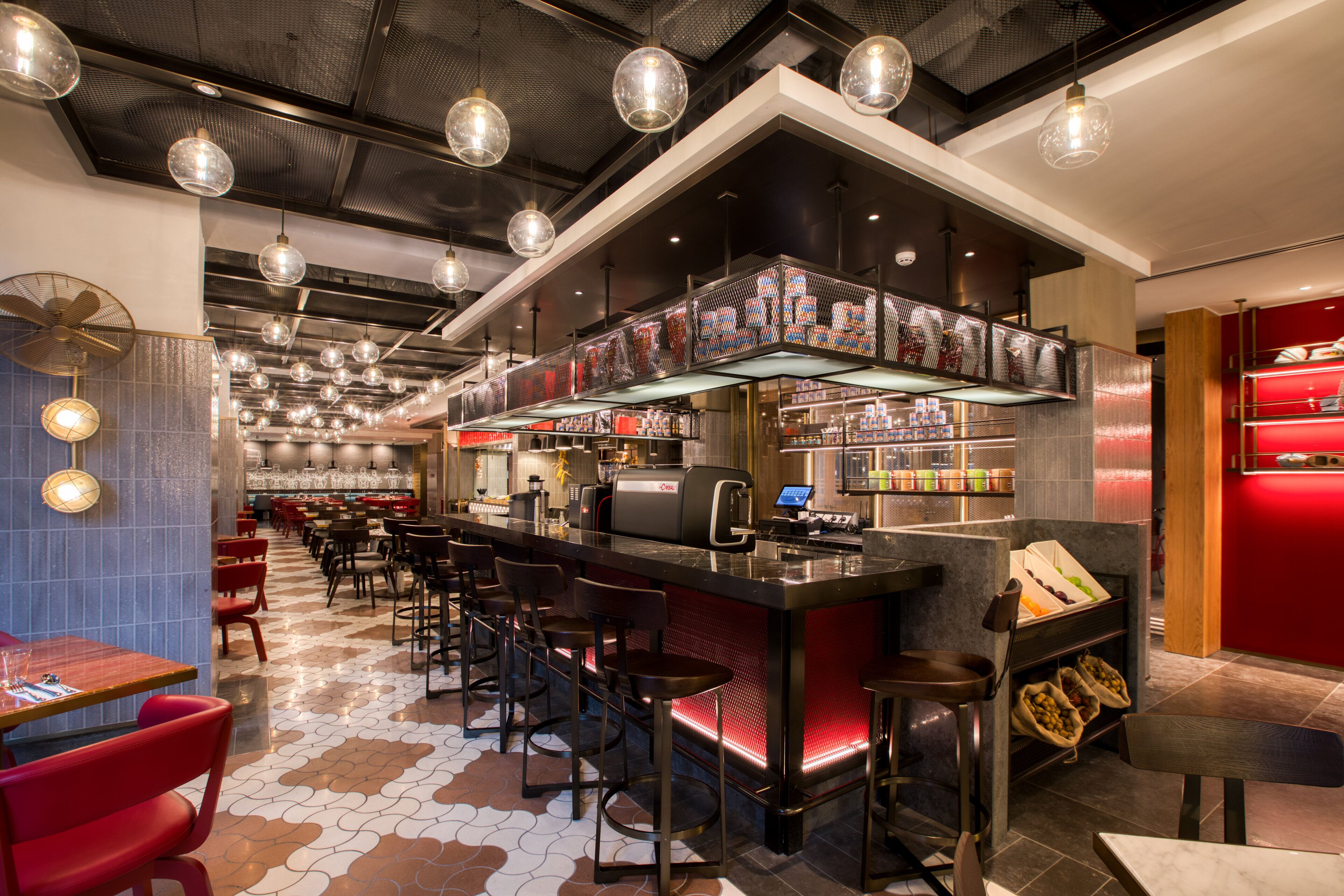 Eine moderne Bar mit einer langen Theke, mehreren Hockern und einer Auswahl an Getränken und Snacks auf Regalen.