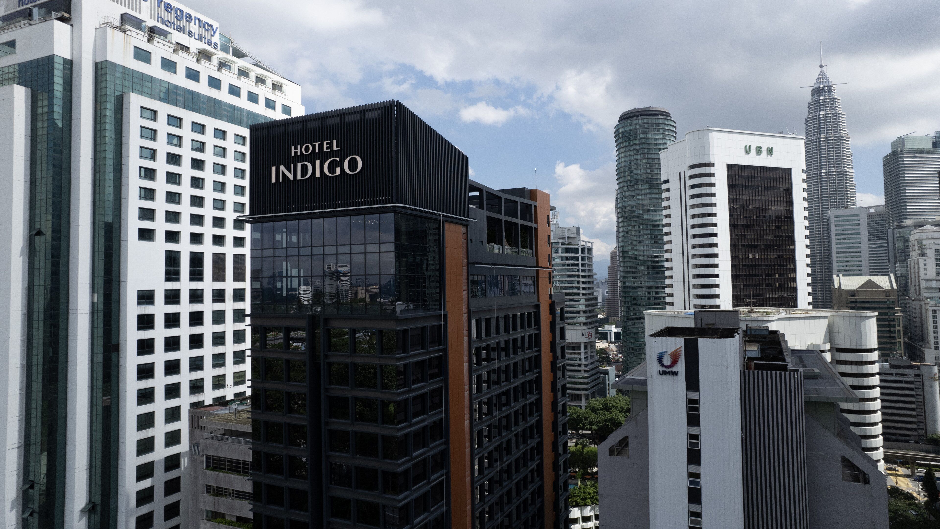 A modern hotel with a prominent 'Hotel Indigo' sign, surrounded by high-rise buildings and a clear sky.