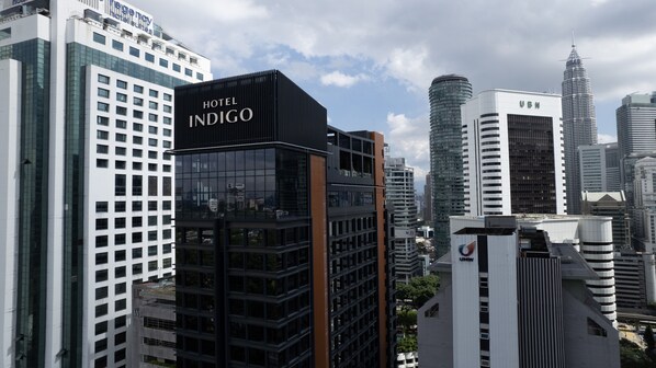 Un hotel moderno con un llamativo letrero de 'Hotel Indigo', rodeado de edificios altos y un cielo despejado.