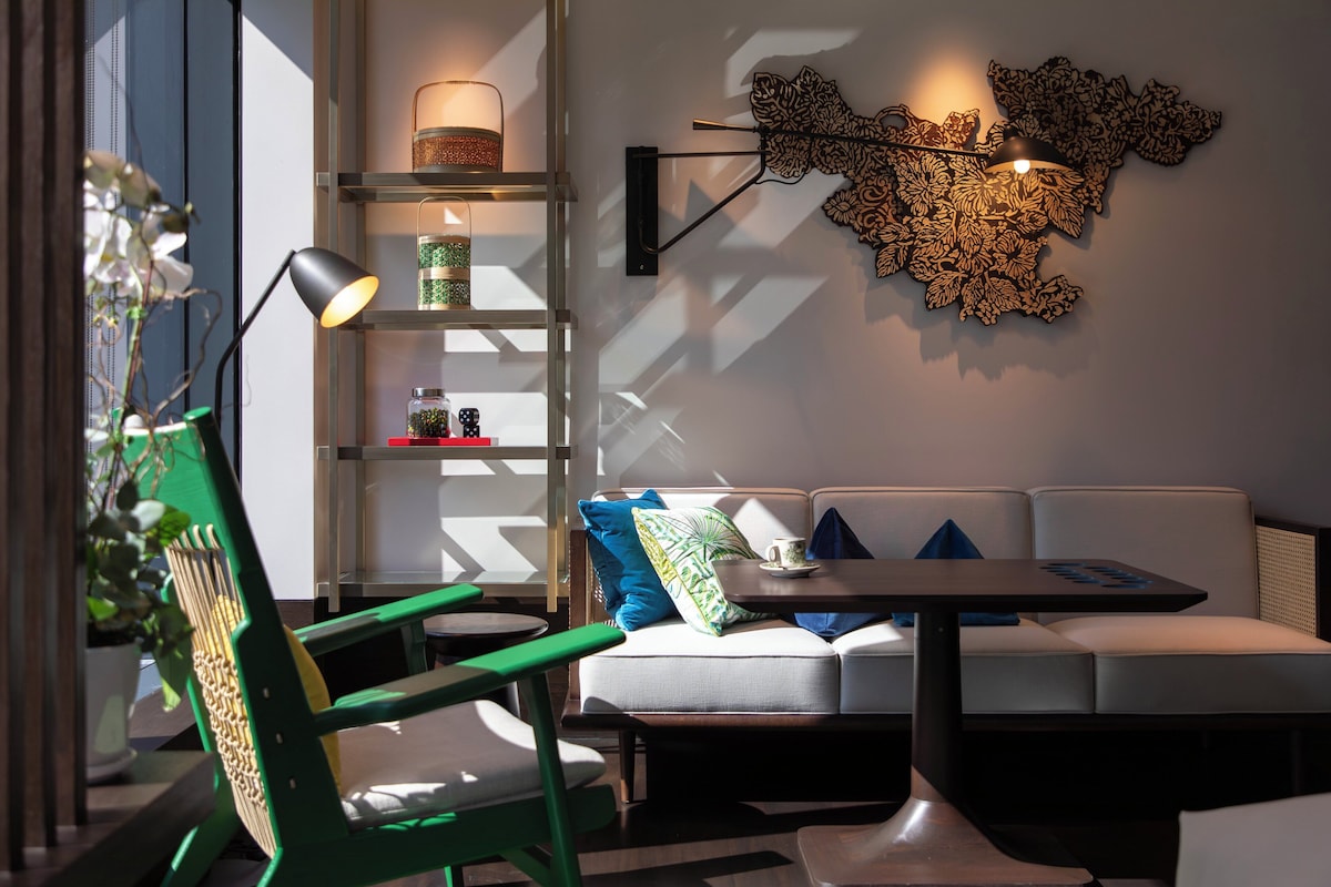 Un salon moderne avec un fauteuil vert, un canapé, une table et des œuvres d’art décoratives au mur.