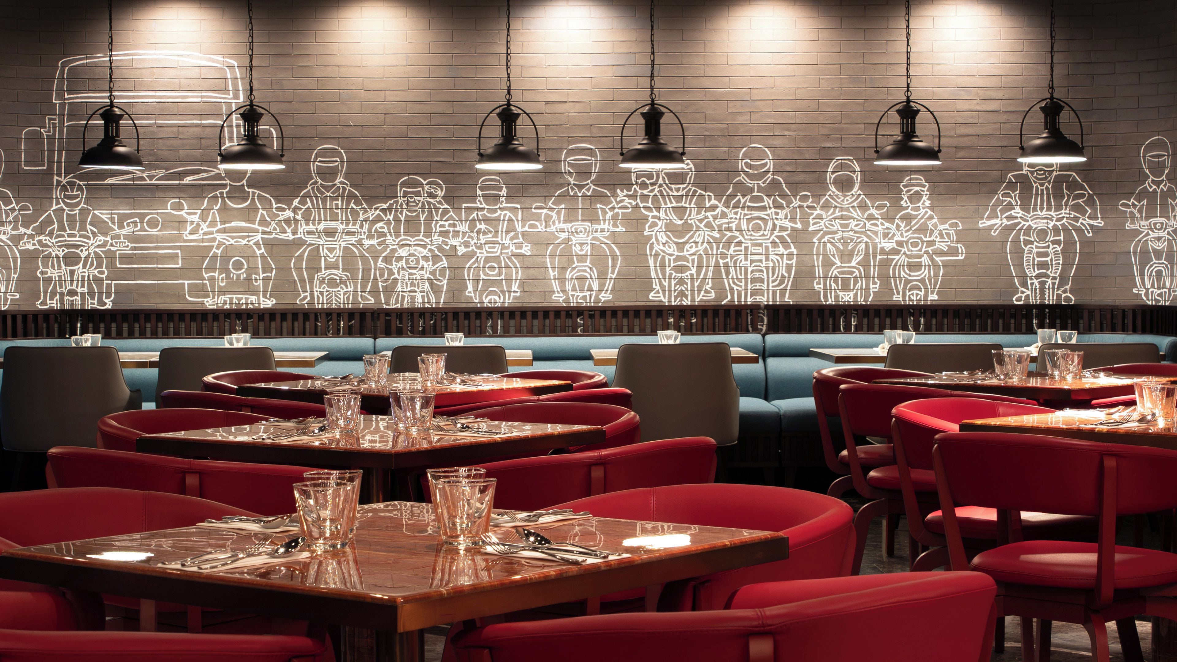 Interior de restaurante con mesas dispuestas para comer, una pared de ladrillo con dibujos lineales iluminados y lámparas colgantes.