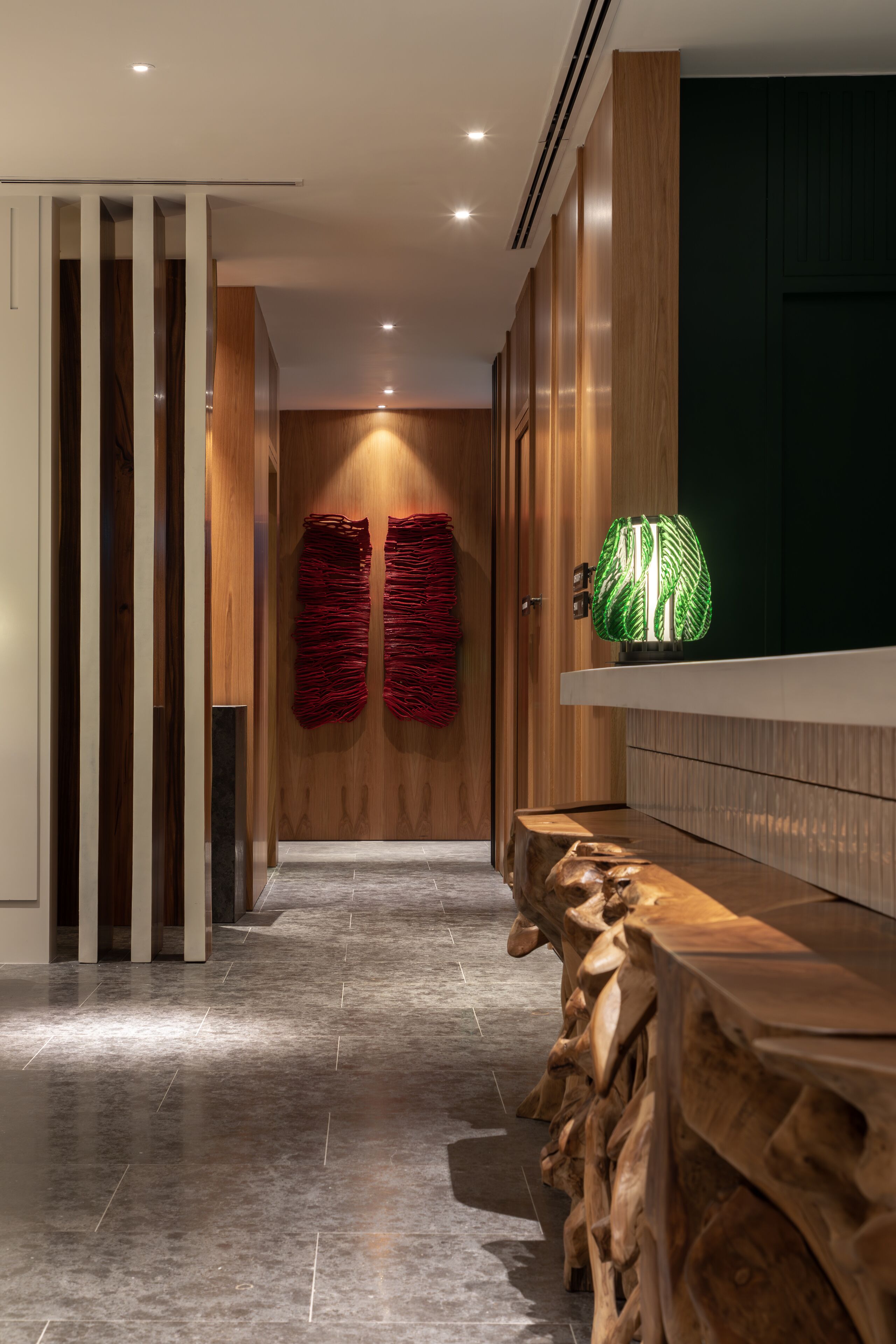 Un pasillo moderno con suelo de madera, un banco de madera y una lámpara decorativa verde.