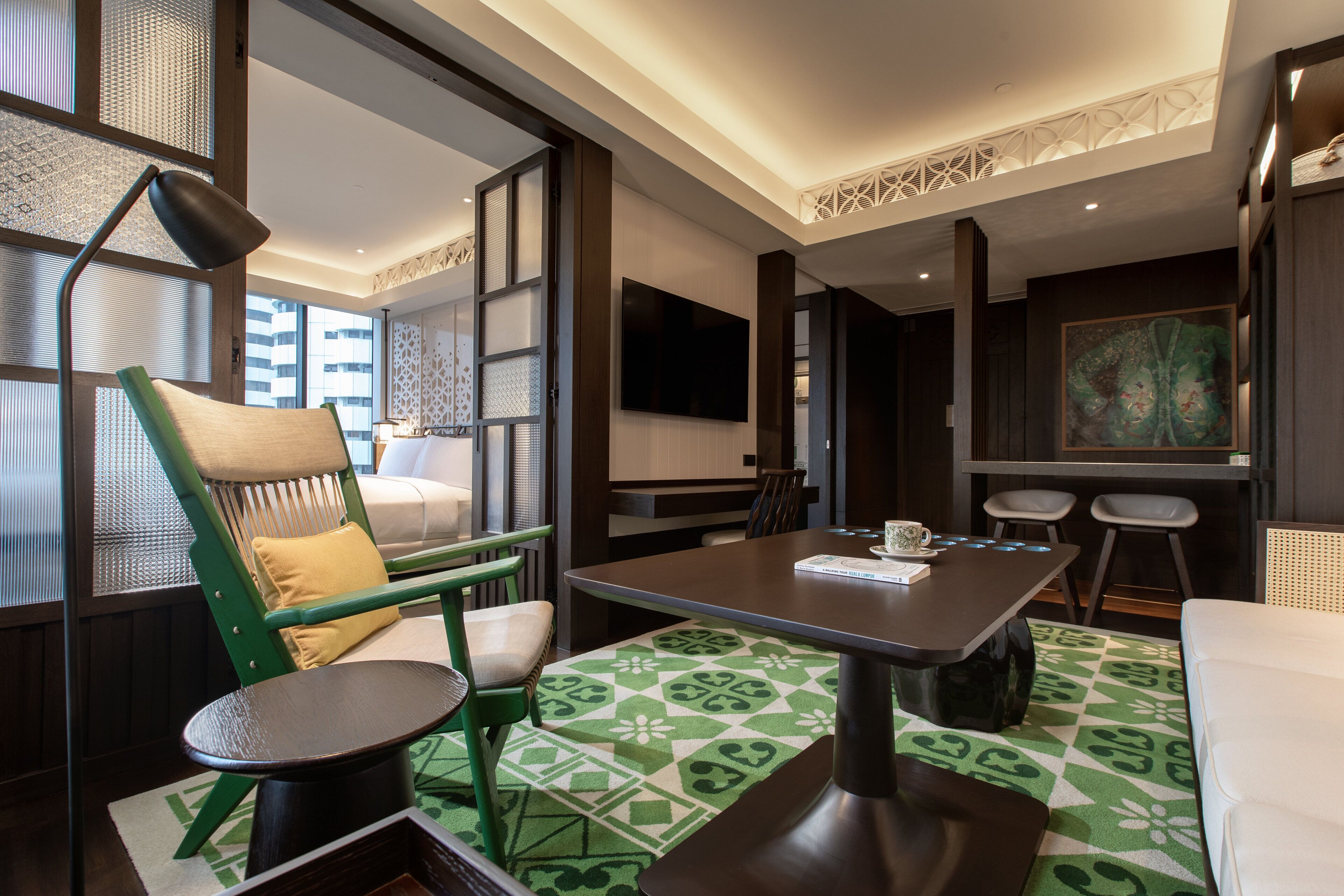 Una habitación de hotel moderna con comedor, una silla verde, una pequeña mesa redonda y un cuadro grande en la pared.
