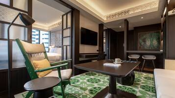 Una habitación de hotel moderna con comedor, una silla verde, una pequeña mesa redonda y un cuadro grande en la pared.