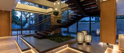 A modern interior with a wooden staircase, large windows, and hanging plants.