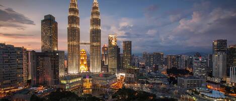 A cityscape with the Petronas Towers prominently illuminated against a twilight sky.