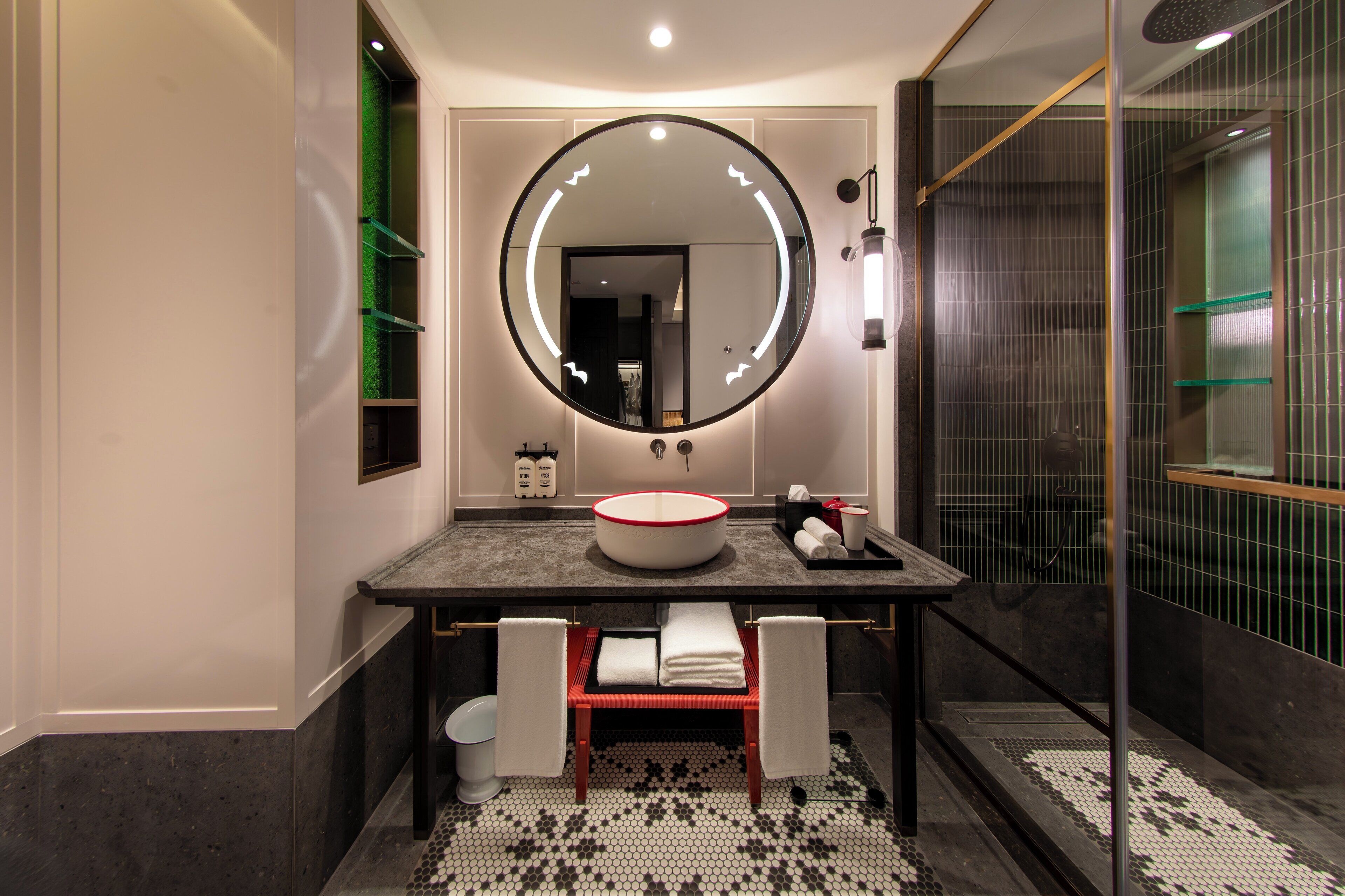 Une salle de bain moderne avec un miroir rond, un lavabo rond et une cabine de douche en verre.