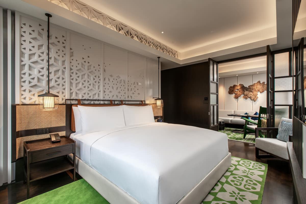 A modern hotel room with a large bed, a desk, a chair, and a decorative wall panel.