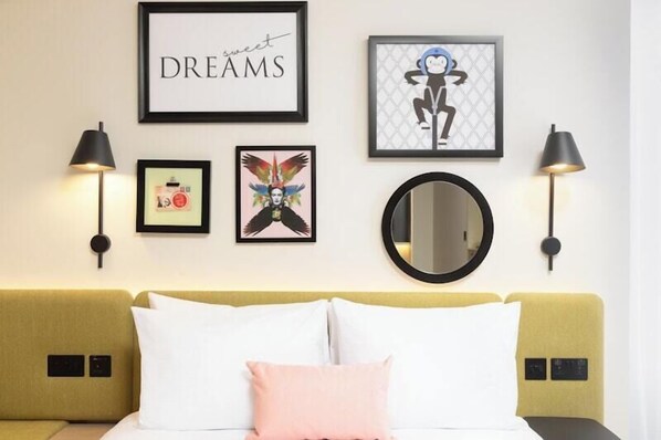 A hotel room with a bed, a wall-mounted mirror, framed artwork, and two wall-mounted lamps. - Hampton by Hilton London Old Street (London)