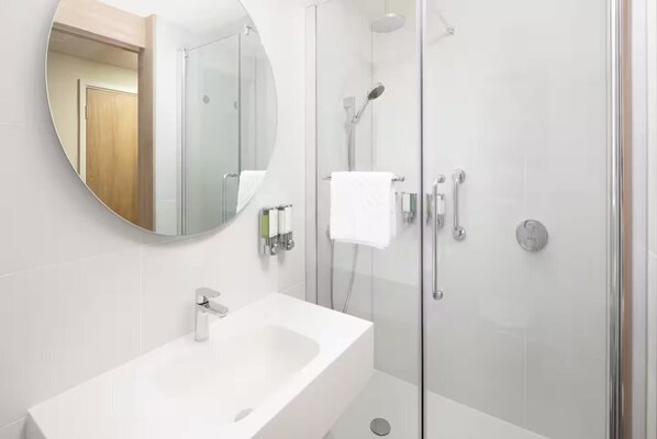 A modern bathroom with a glass-enclosed shower, a white sink, and a round mirror. - Hampton by Hilton London Old Street (London)