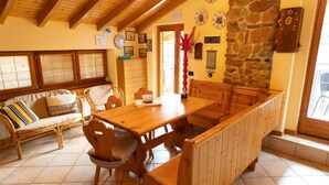A cozy dining area with a wooden table, chairs, and a bench. There are framed pictures on the walls and a stone wall in the background. - [Apartment in the Romantic Courtyard] Lake Lugano (Brusimpiano)