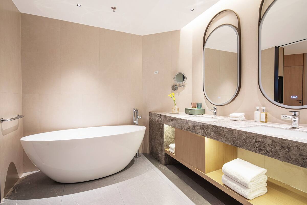Un baño moderno con una bañera independiente, un tocador de mármol y dos espejos montados en la pared.