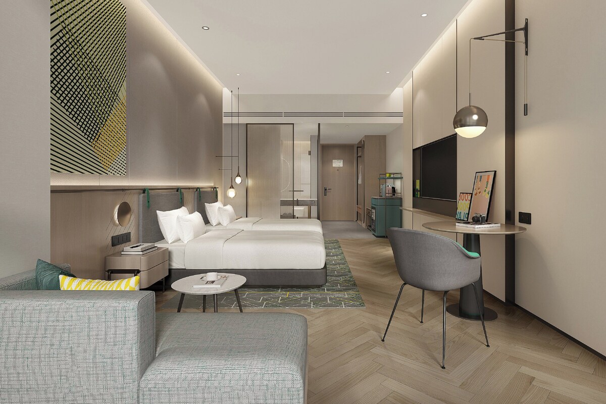 A modern hotel room with a bed, a sofa, a desk, and a TV.