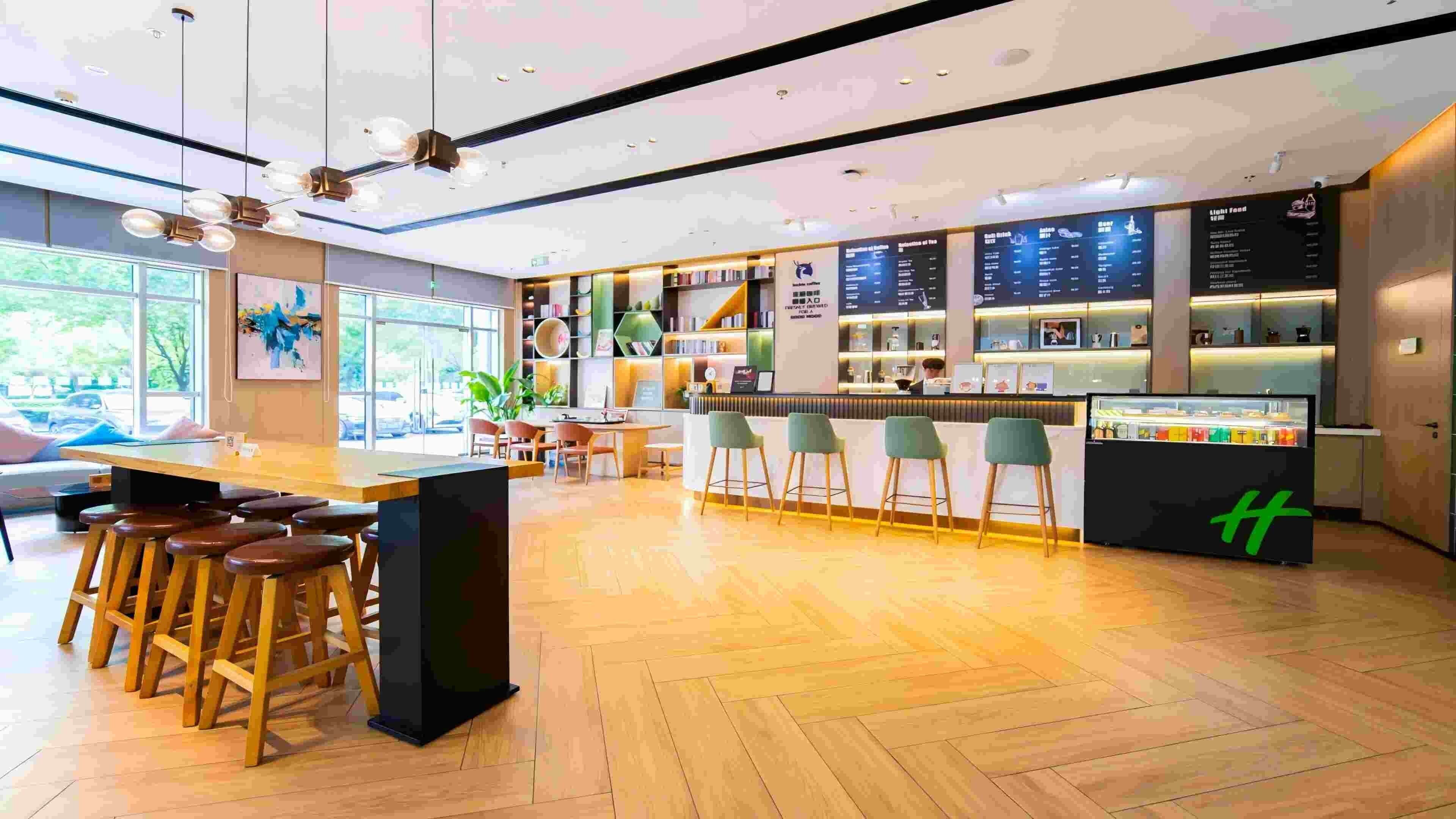 A modern bar area with wooden flooring, bar stools, and a counter with a green logo.