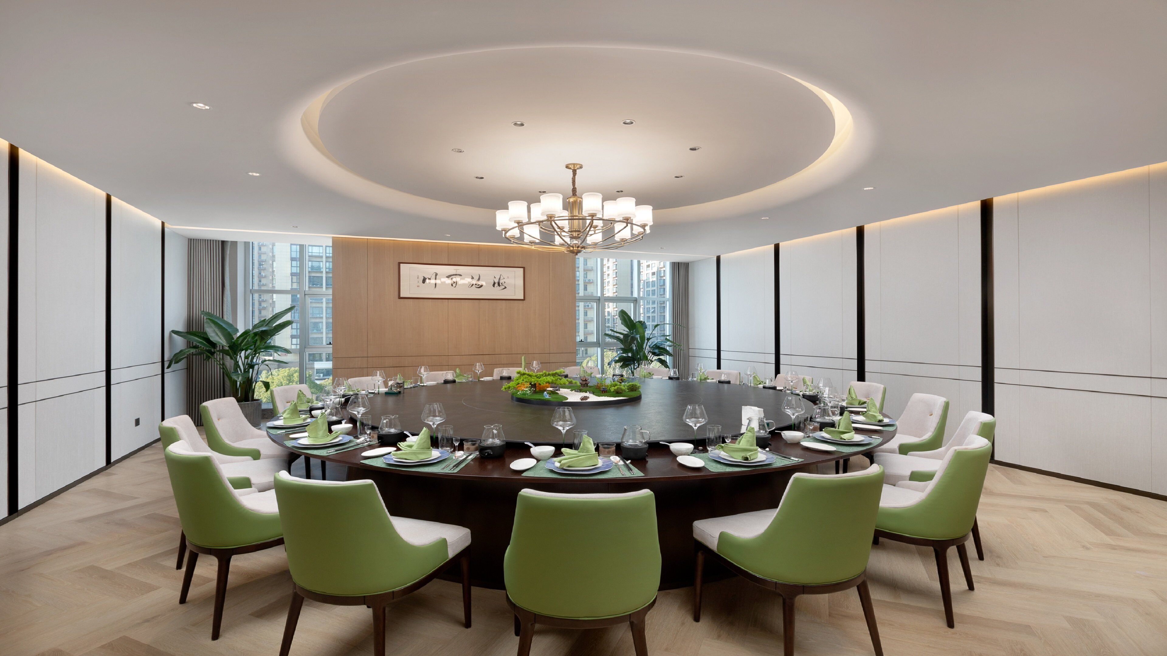 A conference room with a round table, green chairs, and a chandelier.