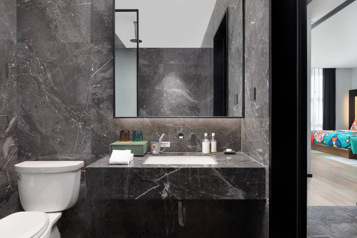 Un baño moderno con lavamanos de mármol, inodoro y espejo grande.