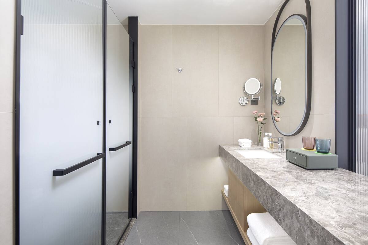 Un baño moderno con mampara de vidrio, encimera de mármol, un espejo grande y un perchero para toallas.