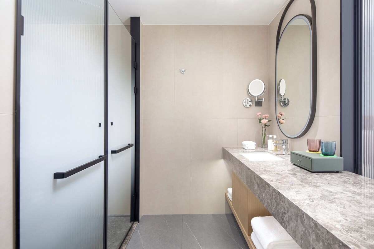 A modern bathroom with a glass shower enclosure, a marble countertop, a large mirror, and a vanity with toiletries.