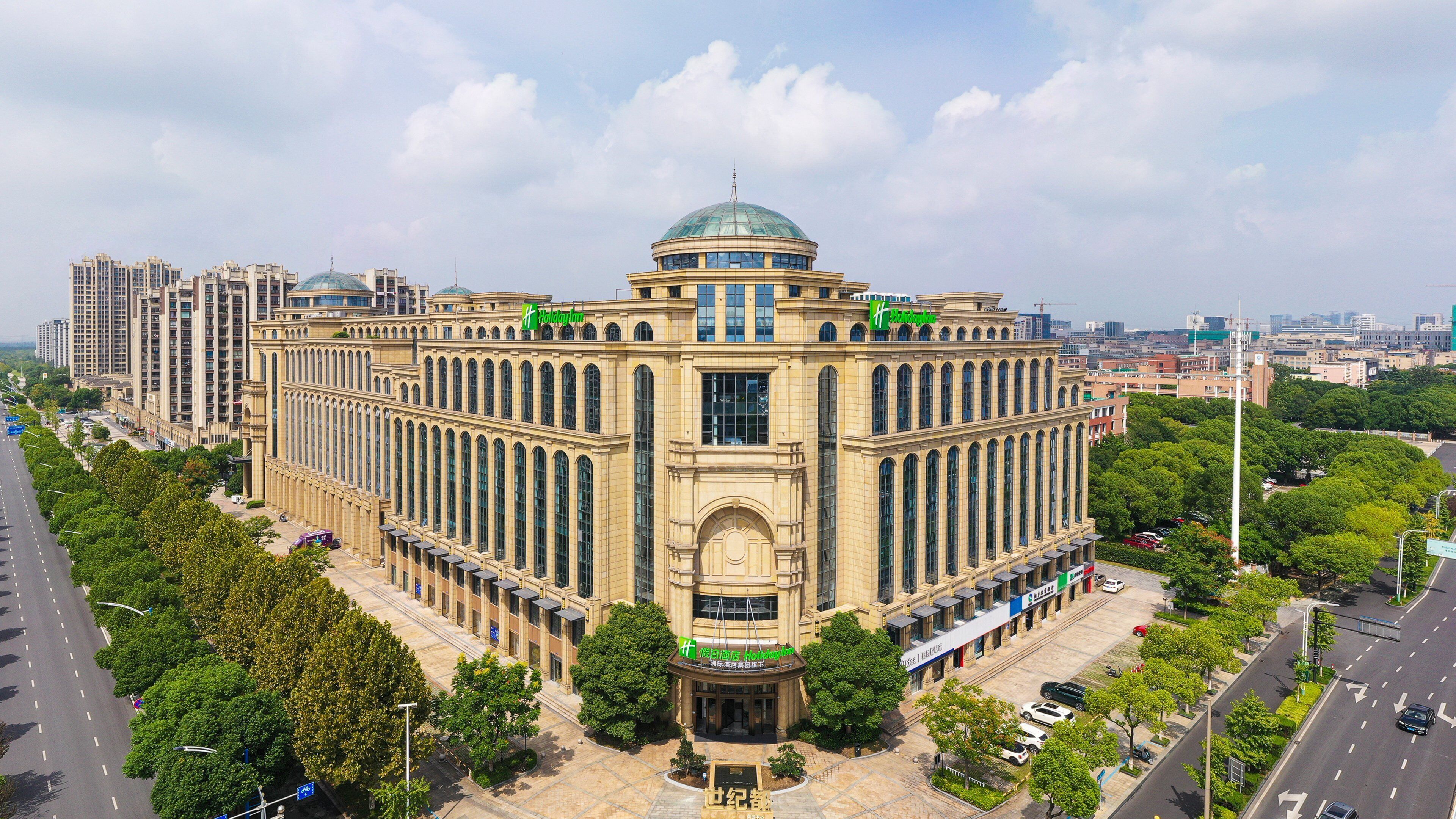 A large, historic building with a central dome and multiple wings, surrounded by trees and modern high-rise buildings.