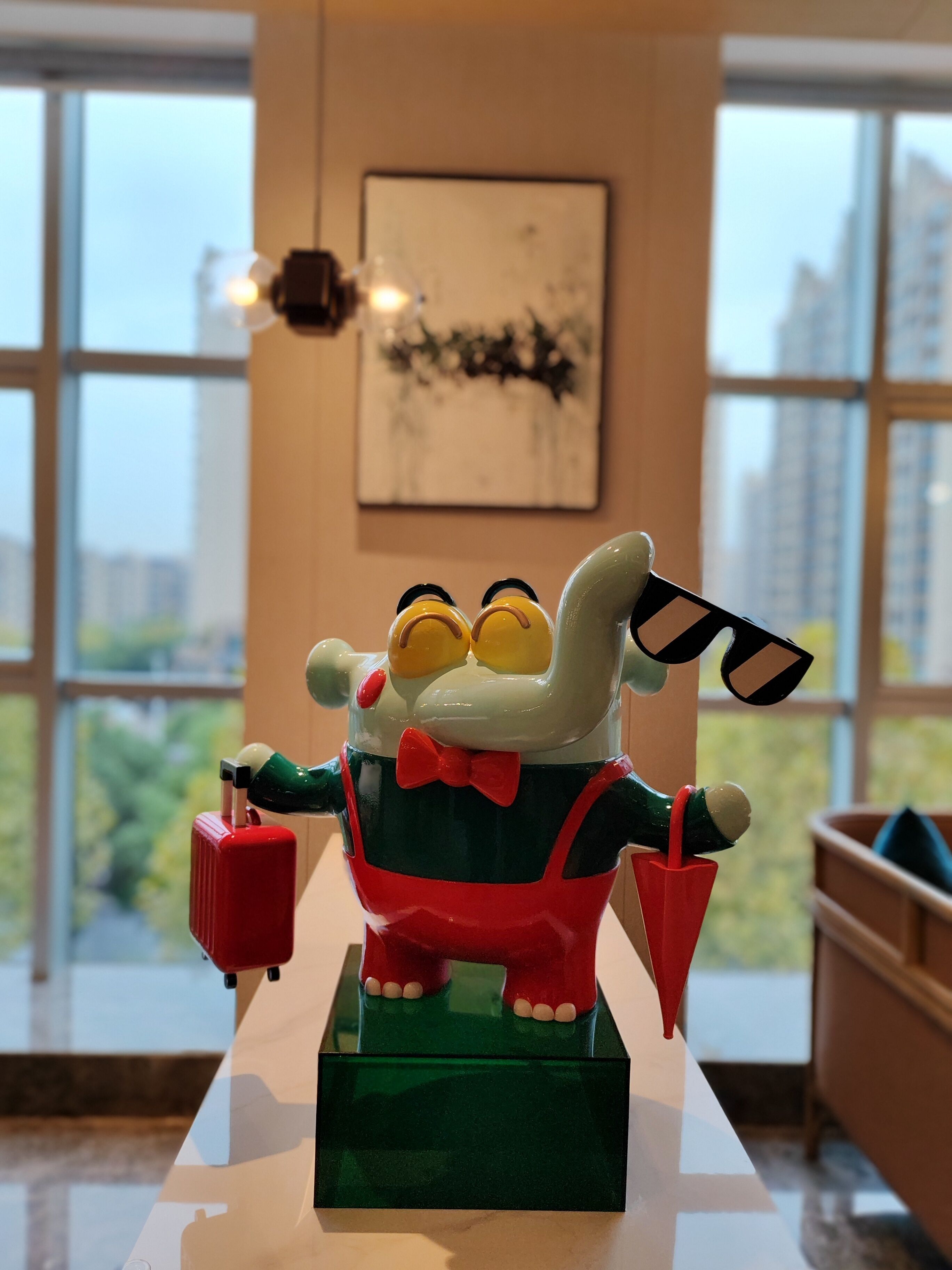 Eine Spielzeugfigur steht auf einem Tisch in einem Raum mit großen Fenstern und einem gerahmten Bild an der Wand.