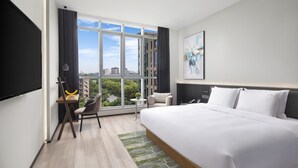 A modern hotel room with a large bed, a desk with a chair, a small table, and a view of the city through large windows. - Holiday Inn TongXiang by IHG (Jiaxing)